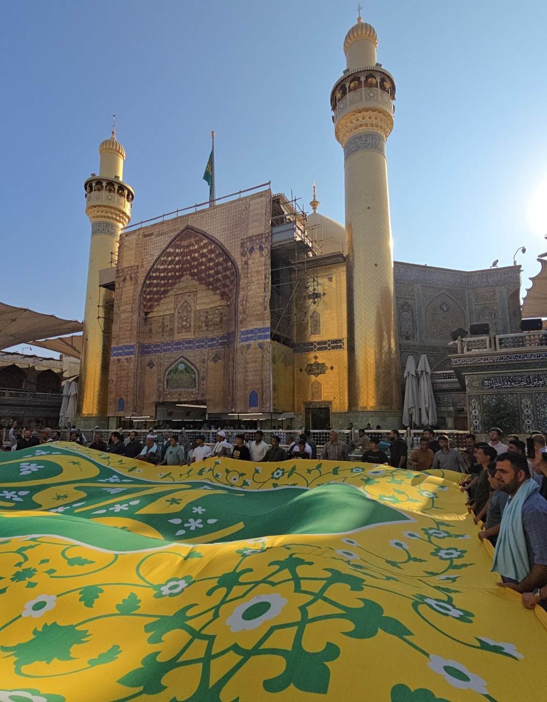 پرچم های مهمونی ده کیلومتری غدیر در حرم امیرالمومنین(ع) متبرک شدند